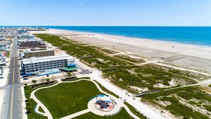 An aerial view of a coastal hotel with a beachfront, a parking lot, and a landscaped area with a circular garden. - Armada By-the-Sea (Wildwood Crest)