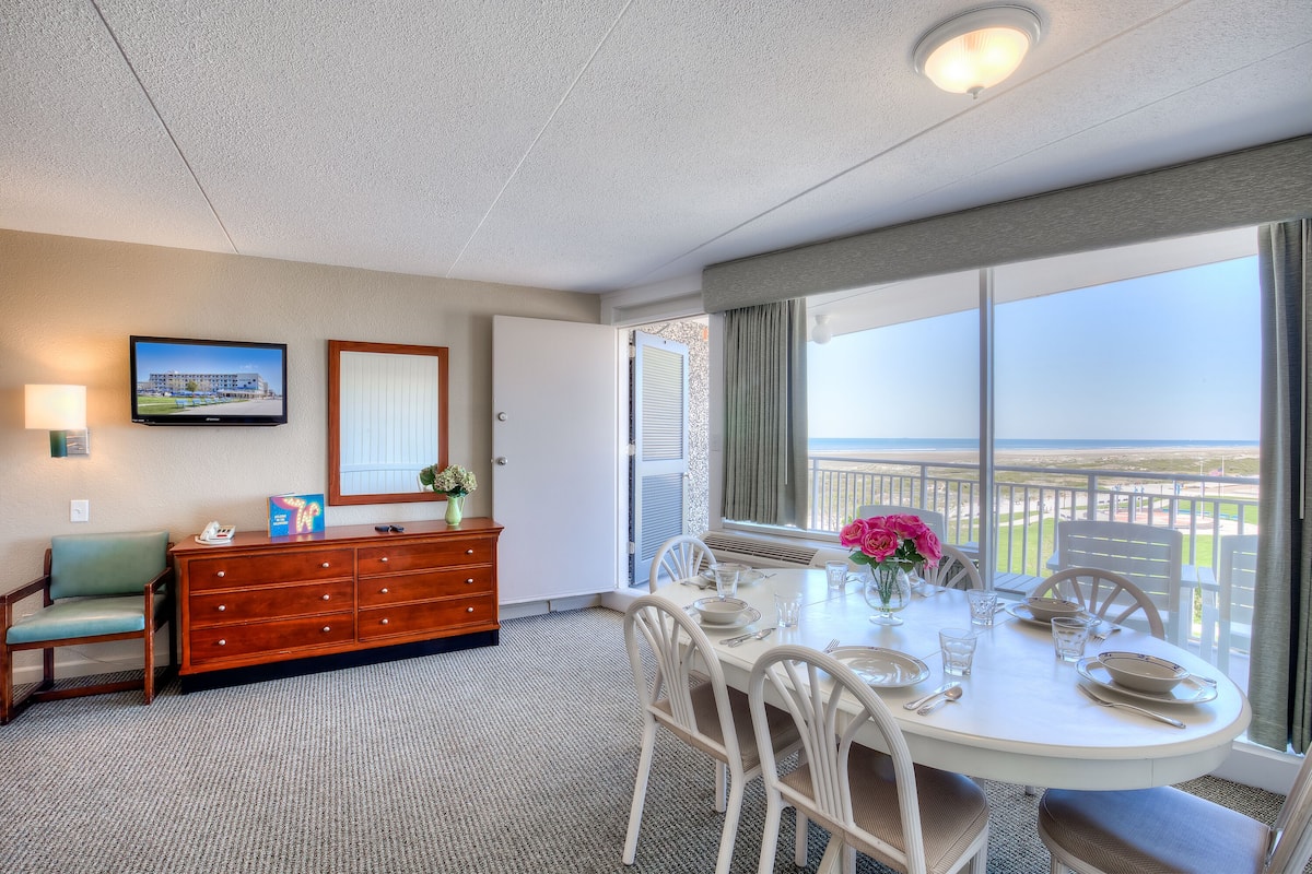 Hotelkamer met een eettafel voor vier personen, een houten dressoir, een televisie aan de muur en een balkon met uitzicht.