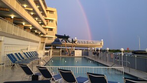 A pool area with lounge chairs, a covered seating area, and a building with balconies. - Armada By-the-Sea (Wildwood Crest)