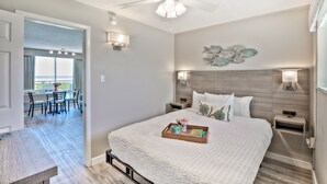 A hotel room with a large bed, a ceiling fan, a dining area with a table and chairs, and a balcony with a view. - Armada By-the-Sea (Wildwood Crest)