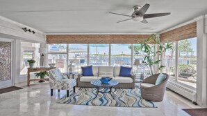 A spacious living area with a ceiling fan, a sofa set, a coffee table, and a view of the beach through large windows. - Armada By-the-Sea (Wildwood Crest)