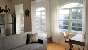 A modern living room with a grey sofa, a wooden dining table, and a large window with a view of palm trees. - SPACIOUS SOBE CORNER ONE BEDROOM---EXCELLENT LOCATION (Miami Beach)