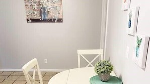 A dining area with a round table and four white chairs, a potted plant on the table, and a wall with framed artwork. - St. Elmo Abode-3 mi to Ruby Falls (Chattanooga)