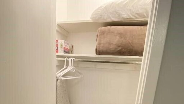 Een inloopkast met houten vloer, een kledingrek en een plank met een opgevouwen handdoek en een doos.