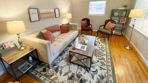 A living room with a sofa, two armchairs, a coffee table, and a rug. There are lamps on side tables, a bookshelf, and a window with blinds. - St. Elmo Abode-3 mi to Ruby Falls (Chattanooga)