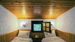 A small, cozy room with two beds, wooden walls, a window with a view, and a lamp on a nightstand.