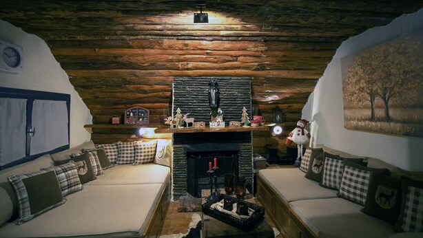 A cozy log cabin interior with a fireplace, wooden walls, and a sofa with plaid cushions.