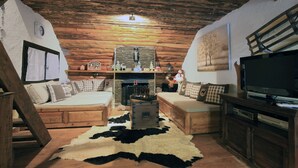 A cozy log cabin interior with a fireplace, wooden furniture, and a television.