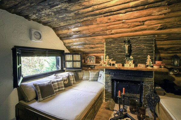 Une chambre chaleureuse dans un chalet en rondins, avec un lit, une cheminée et une fenêtre donnant sur un paysage verdoyant.