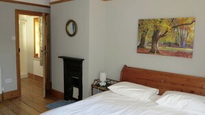 A bedroom with a wooden headboard, a bed with white linens, a nightstand with a lamp, a painting of trees, and a mirror on the wall. - Large Arts & Crafts Cottage with 7 bedrooms  in Lymington near the coast (Lymington)