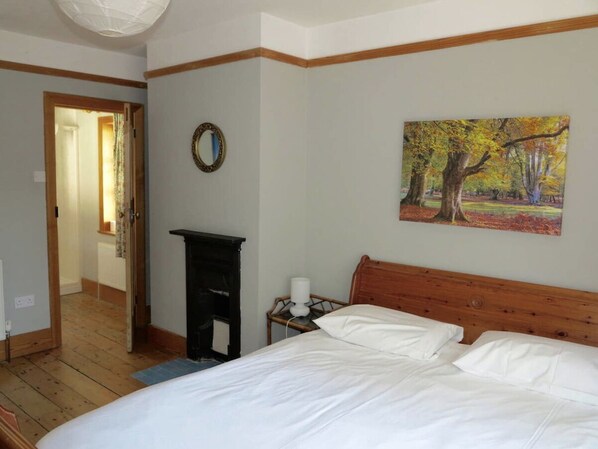 Ein Schlafzimmer mit einem Holzkopfende, einem Bett mit weißer Bettwäsche, einem Nachttisch mit Lampe, einem Baumgemälde und einem Spiegel an der Wand.