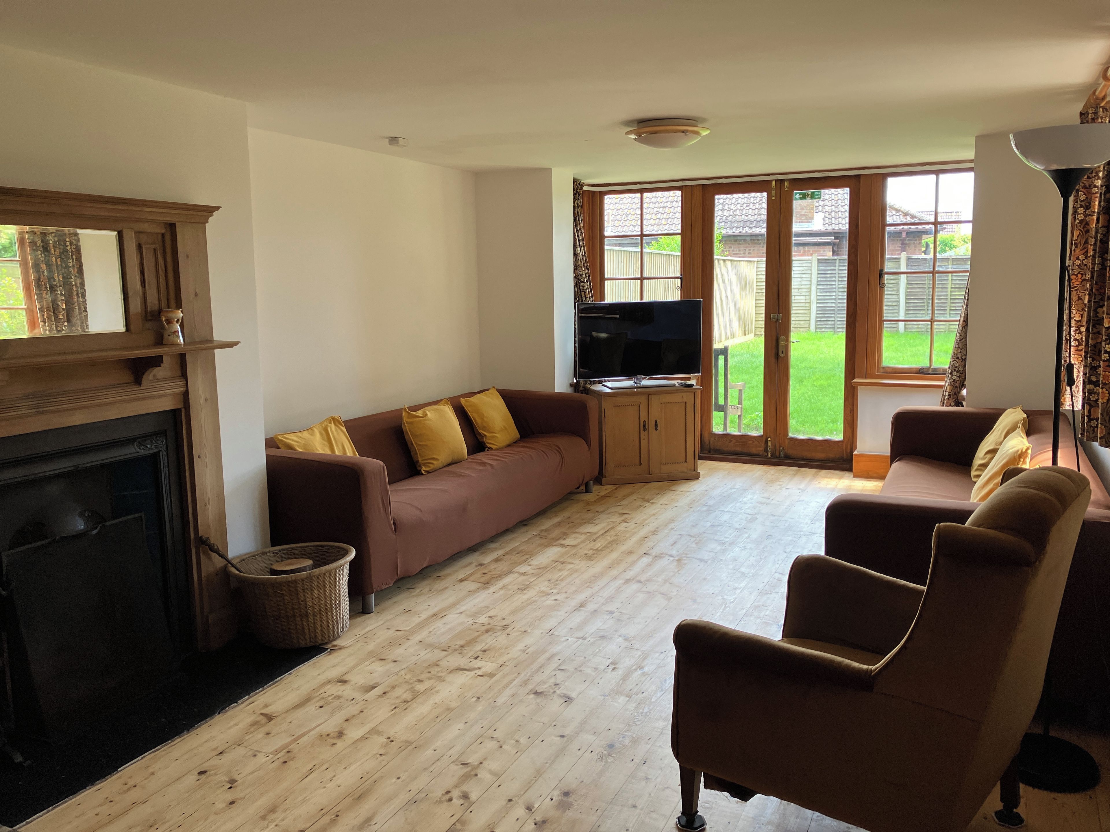 A living room with a fireplace, a sofa set, a television, and a view of the outdoors through large windows.