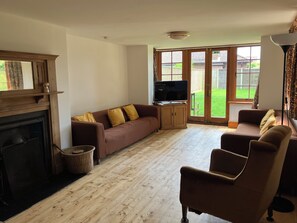 A living room with a fireplace, a sofa set, a television, and a view of the outdoors through large windows. - Large Arts & Crafts Cottage with 7 bedrooms  in Lymington near the coast (Lymington)
