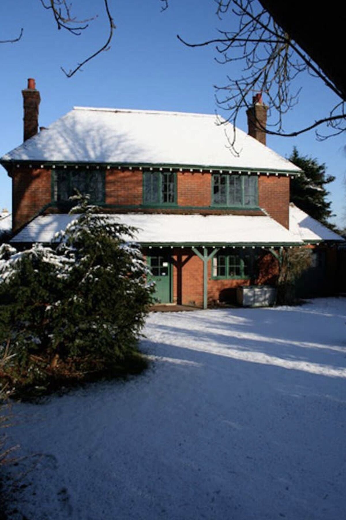 Una casa de ladrillo de dos pisos, con una puerta y ventanas verdes, rodeada de nieve.