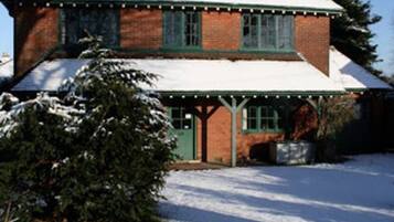 Una casa de ladrillo de dos pisos, con una puerta y ventanas verdes, rodeada de nieve.