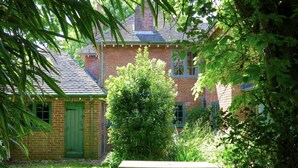 A brick house with a green door and windows, surrounded by lush greenery and a picnic table in the foreground. - Large Arts & Crafts Cottage with 7 bedrooms  in Lymington near the coast (Lymington)