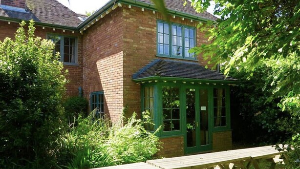 A brick house with a green window frame and a wooden picnic table in front. - Large Arts & Crafts Cottage with 7 bedrooms  in Lymington near the coast (Lymington)