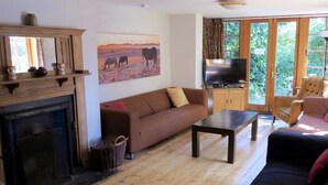 A living room with a fireplace, a sofa, a television, and a large window with a view of greenery. - Large Arts & Crafts Cottage with 7 bedrooms  in Lymington near the coast (Lymington)