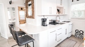 Une cuisine moderne avec des meubles blancs, un îlot central doté de tabourets de bar, une machine à café et un panneau sur lequel on peut lire : « ALLEZ, PLONGEZ DANS L’OCÉAN ! »