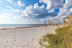 A sandy beach with footprints and seaweed, leading to the ocean under a partly cloudy sky.
