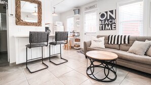 Un salon moderne avec un canapé, deux fauteuils, une table basse et, au fond, un coin cuisine.