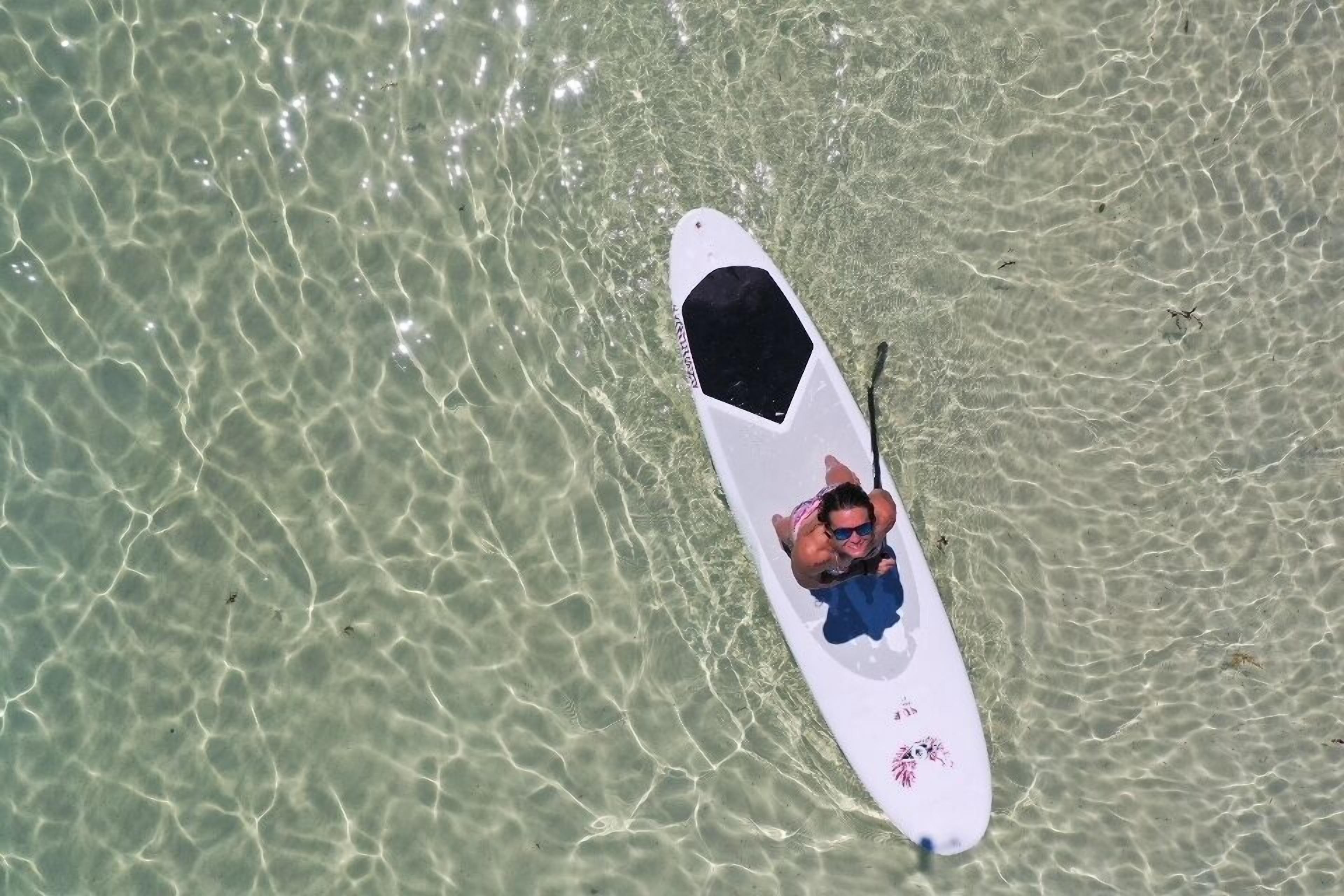 Eine Person liegt auf einem Surfbrett im klaren, flachen Wasser.