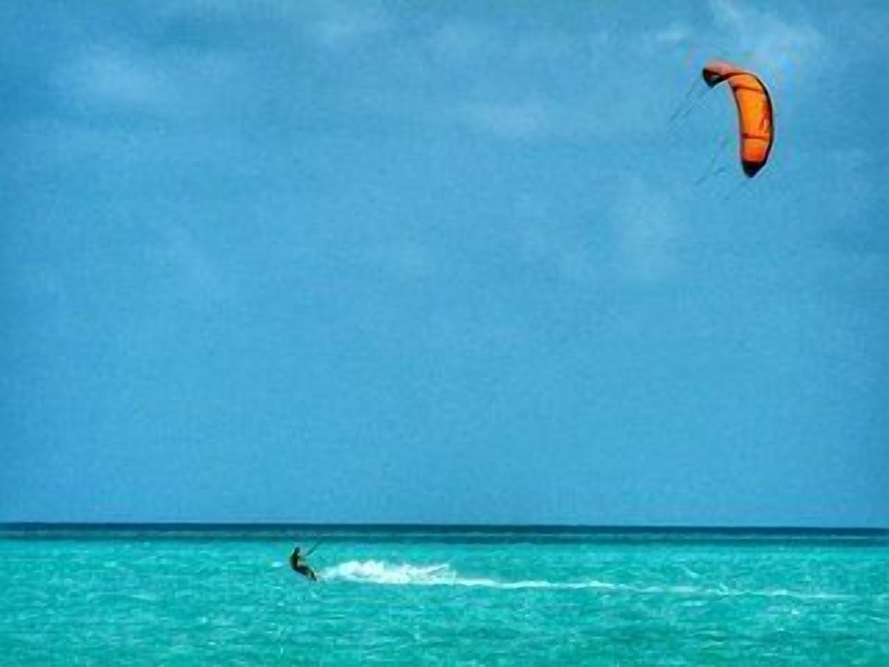 Una persona che pratica windsurf su un'acqua turchese sotto un cielo sereno.