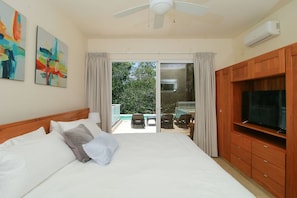 A hotel room with a bed, a TV, a ceiling fan, and a balcony with outdoor furniture.