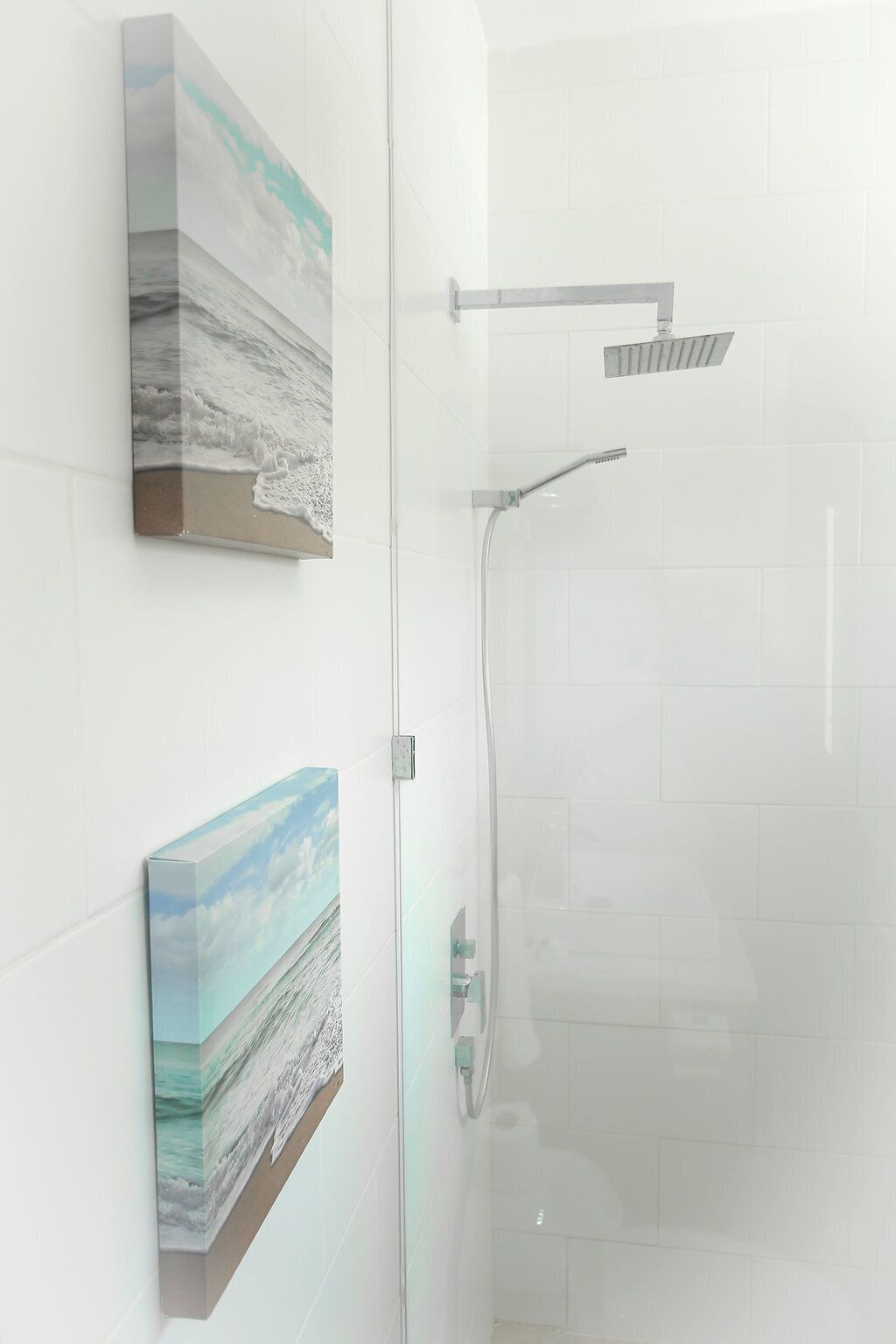 A bathroom with a glass shower enclosure, a handheld showerhead, and two framed artworks on the wall.