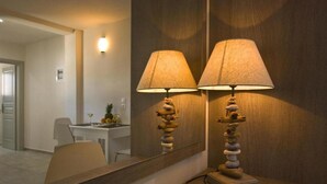 A bathroom with a mirror, two wall-mounted lamps with textured lampshades, and a stone sculpture on the floor. - Alafouzos Studios (Santorini)