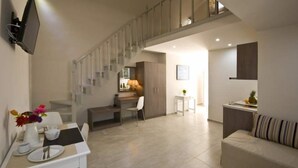 A modern living room with a sofa, a dining table with chairs, a kitchen area, and a staircase. - Alafouzos Studios (Santorini)
