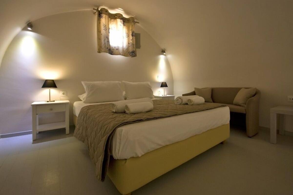 A bedroom with a bed, two bedside tables, a nightstand, a sofa, and a curved ceiling.