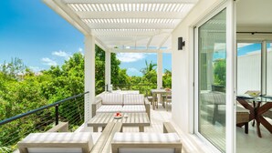 A covered outdoor patio with wooden furniture and glass doors leading to an interior dining area. - Stunning 1BR Ocean Vw + Jacuzzi SUV Kite Boarding - Wyakha 4 Ocean View (Long Bay)