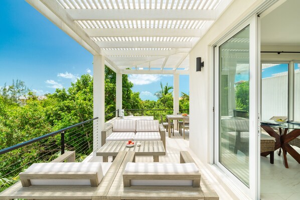 A covered outdoor patio with wooden furniture and glass doors leading to an interior dining area.