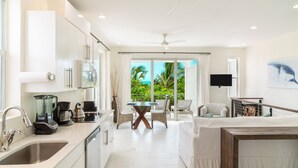A modern kitchen with white cabinetry, a dining area with a glass table, and a living space with a sofa and a TV. - Stunning 1BR Ocean Vw + Jacuzzi SUV Kite Boarding - Wyakha 4 Ocean View (Long Bay)
