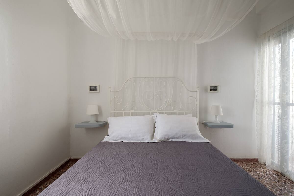 A bedroom with a bed, white curtains, and two bedside lamps.