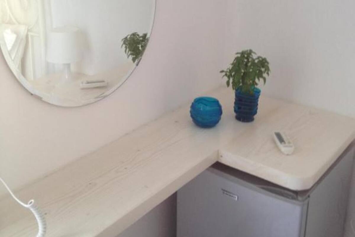 A small, compact room with a white desk, a mirror, a small plant, and a phone on the desk.