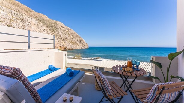 Un balcón con vistas al mar, sillas de descanso, una mesa con aperitivos y una botella de agua.