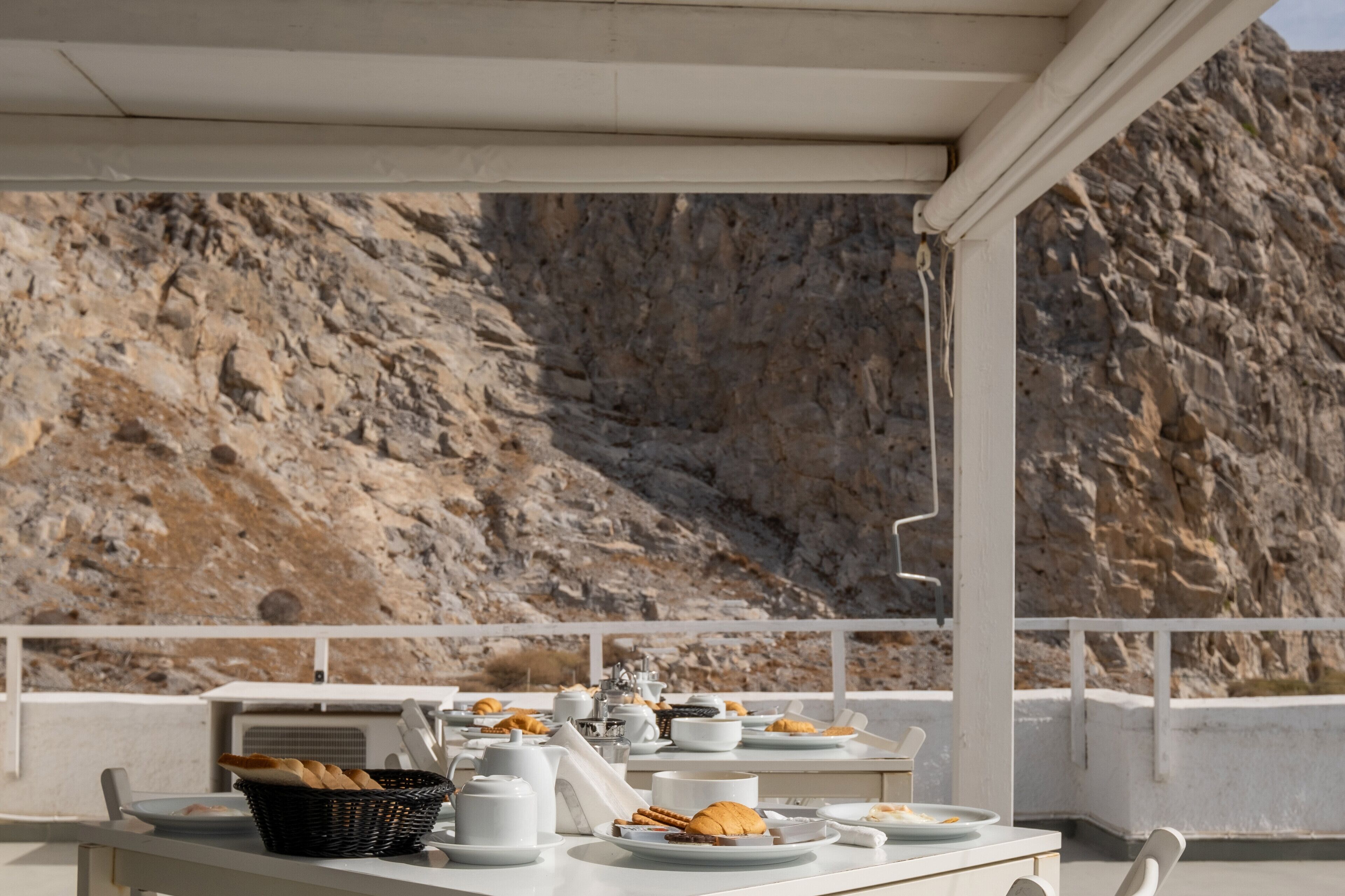 A dining area with a table set for breakfast, overlooking a rocky cliff.