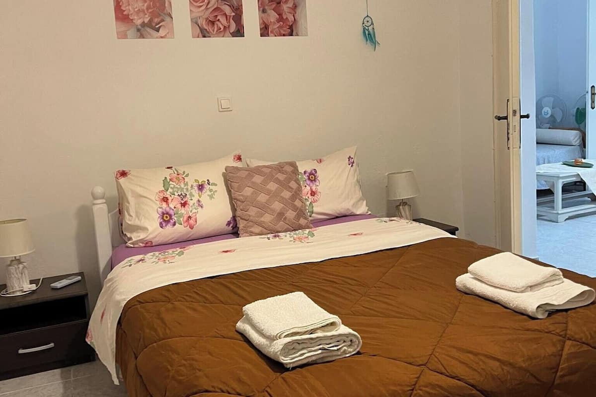 A bedroom with a brown quilted bedspread, floral pillows, and a nightstand with a lamp.