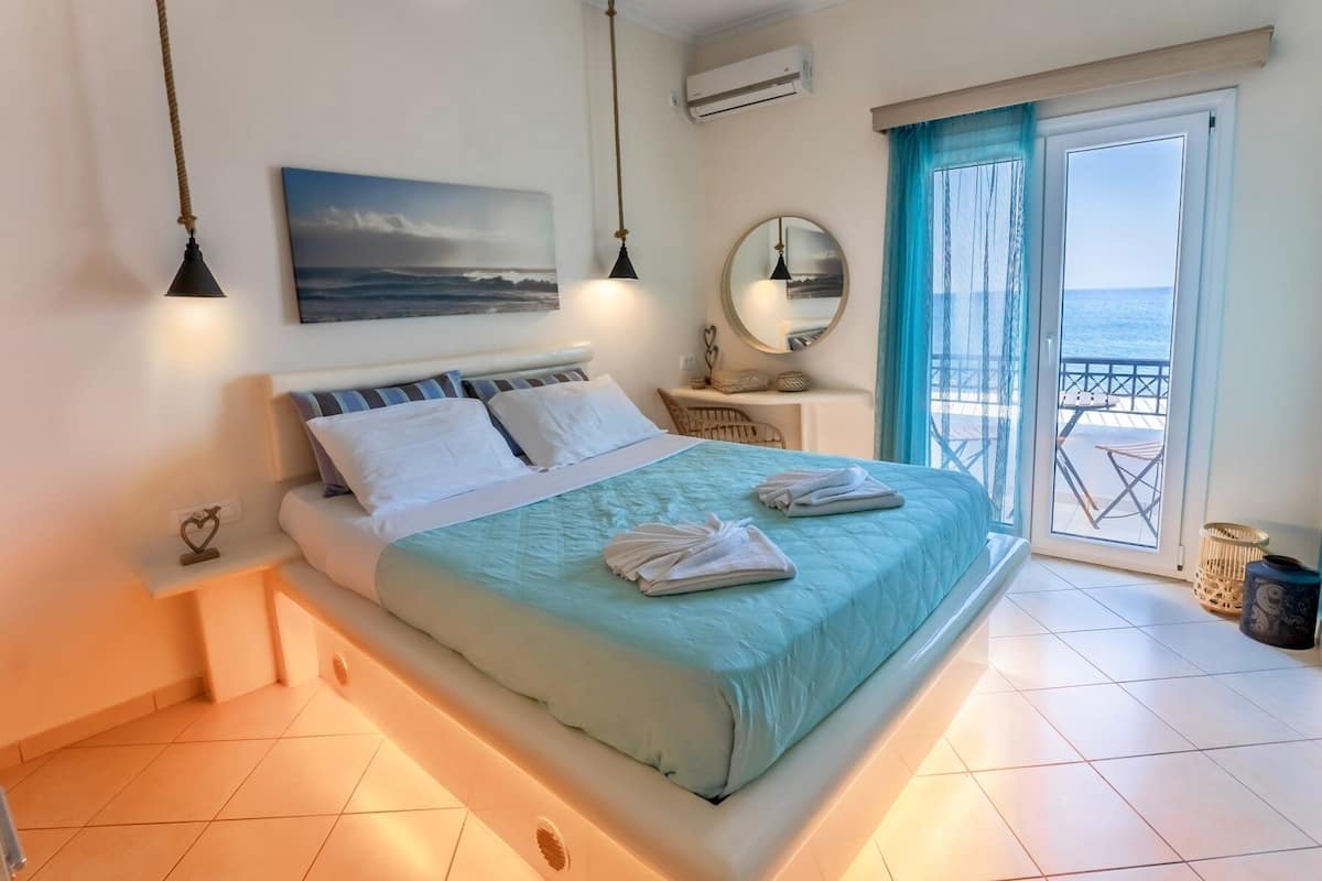 A bedroom with a bed, bedside tables, a mirror, and a view of the sea through a balcony door.