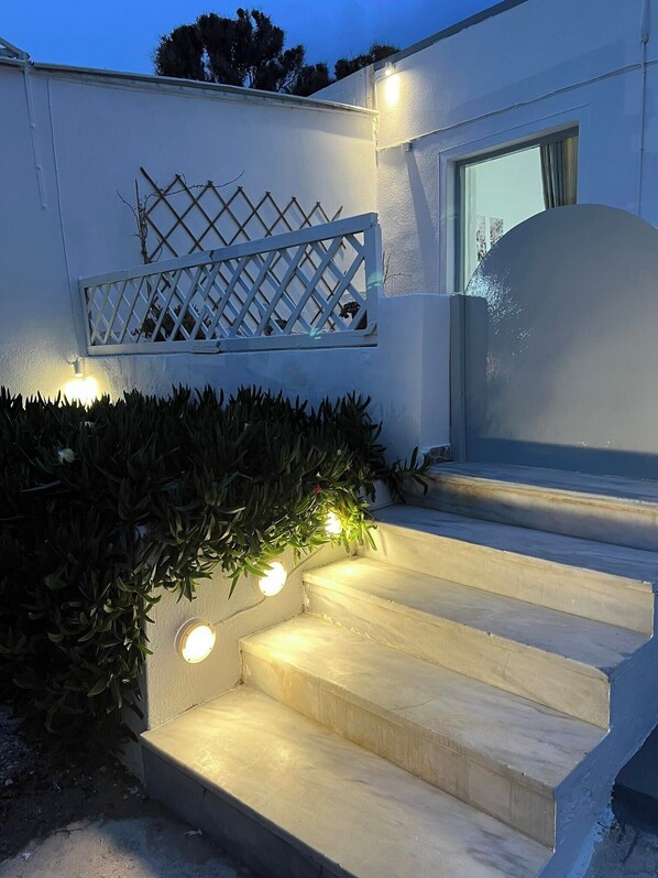 A set of outdoor stairs with a white railing and a lattice design, leading to a door. - Sagma Beach Rooms (Santorini)