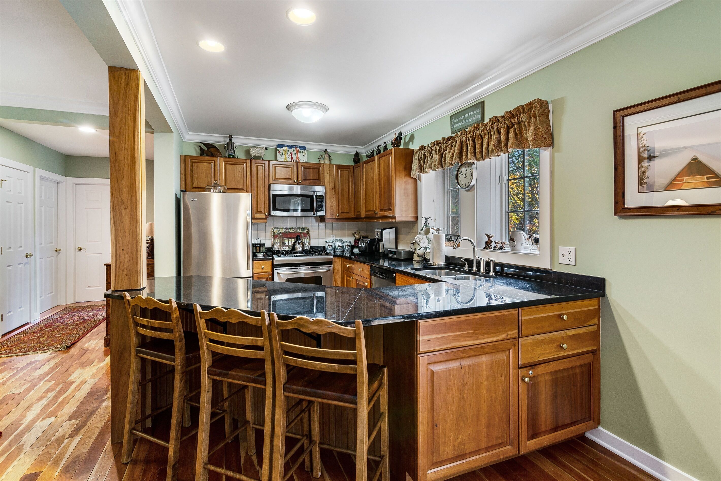 A kitchen with wooden cabinets, a stainless steel refrigerator, a microwave, and a large island with bar stools.