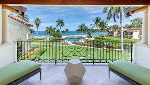A balcony with a view of the ocean and palm trees, featuring a geometric table and two cushioned chairs.