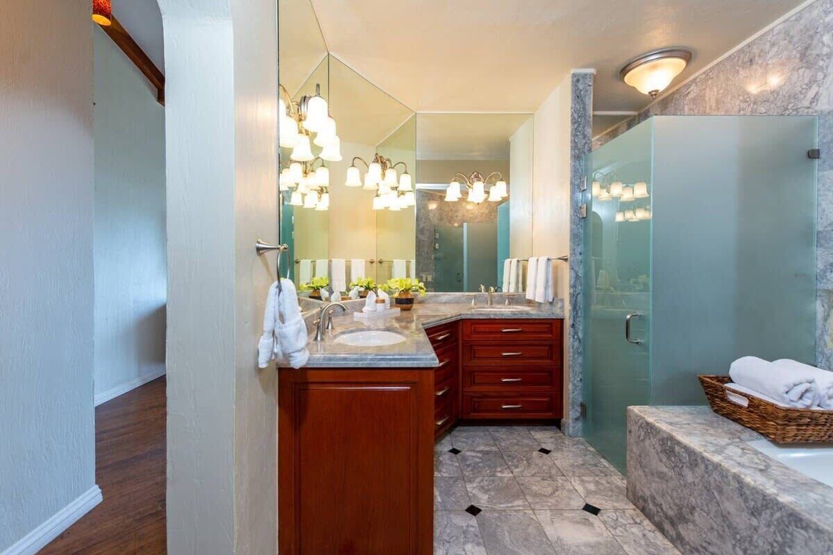 Une salle de bain moderne avec un meuble-lavabo en bois, une cabine de douche en verre et une baignoire surmontée d’un plateau en marbre.