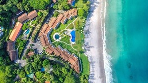 An aerial view of a resort with multiple buildings, a central pool area, and a beach.
