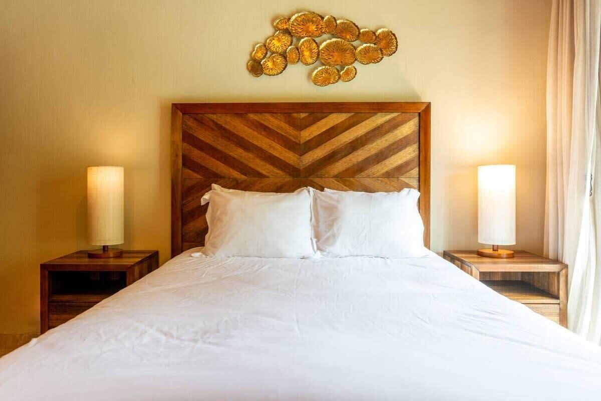Una camera d'hotel con un letto grande, due comodini con lampade, una testiera in legno a motivi a spina di pesce e un elemento decorativo sopra il letto.