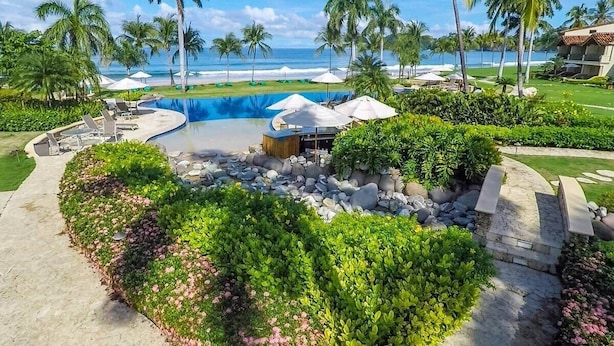 A resort with a swimming pool, palm trees, and a view of the ocean.