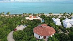A coastal property with a white house, a red-roofed building, and several white structures surrounded by lush greenery and a beach.