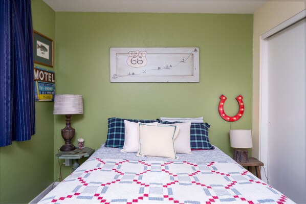 Una cama bien hecha con colcha, un reloj de pared, un letrero enmarcados de la Ruta 66, un caballito de herradura de neón y un letrero de motel.